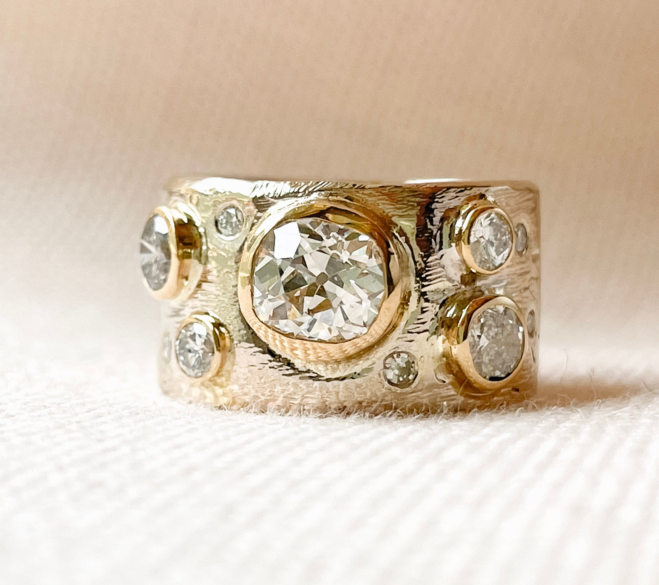 Custom diamond cigar band ring featuring hand-carved texture and bezel-set stones in gold.