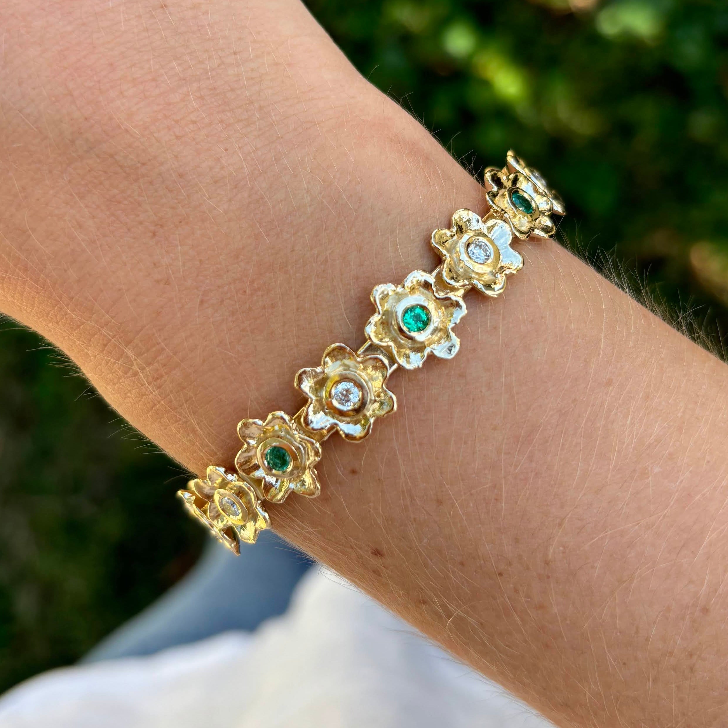 Custom emerald and diamond bracelet featuring hand-carved floral links in gold.