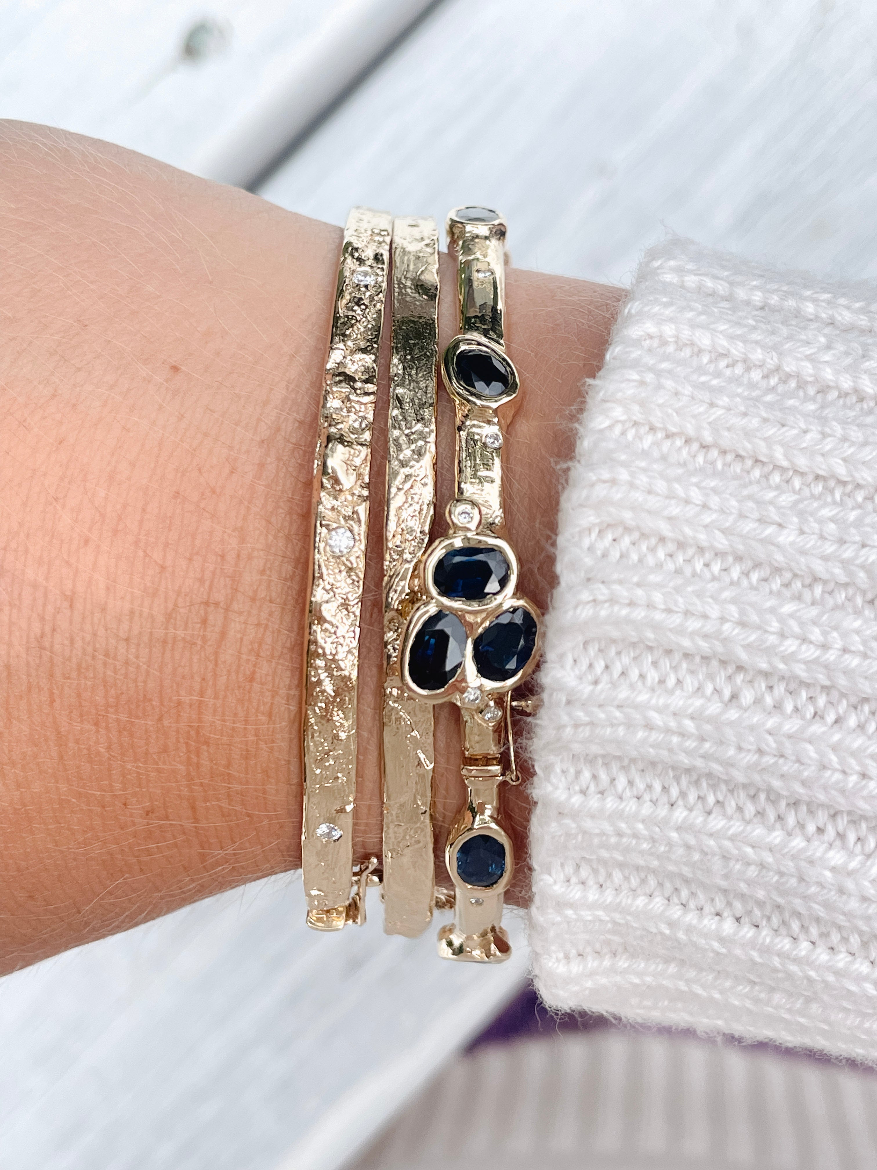 Stack of custom hand-carved gold bangles featuring sapphire and diamond accents.