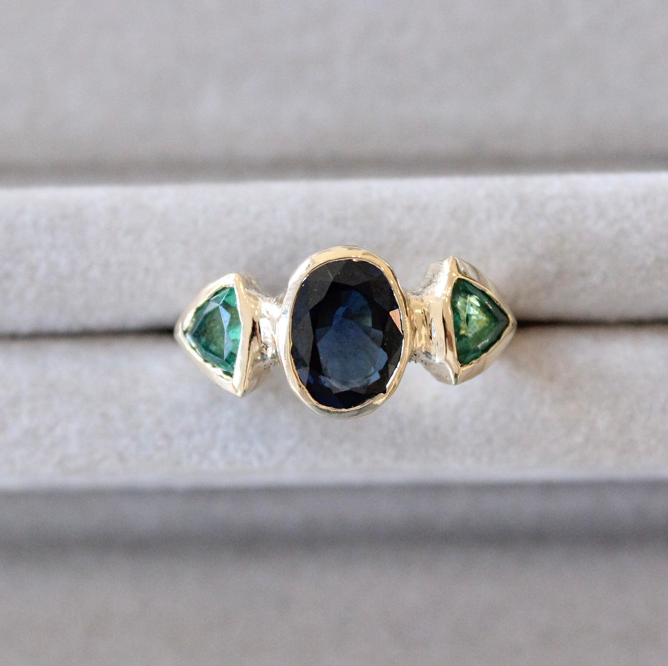 Custom three-stone ring with sapphire and emeralds set in hand-carved gold.
